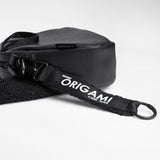 ORIBAGU（折り紙バッグ）のライオン型ミニバッグに、別売りの「ORIGAMI」ロゴ入りストラップを取り付けた状態の写真。バッグの黒レザーとストラップの黒ボアの素材の違いや、黒の金具（カラビナ）が確認できる。デザイン性と実用性の高さを強調したスタイリング写真。